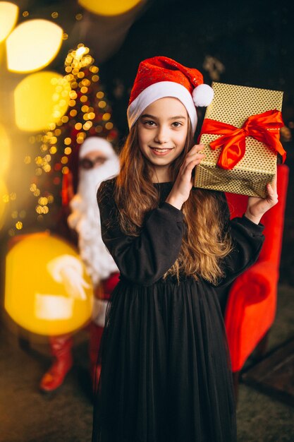 Menina com caixa de presente e santa no fundo sentado no sofá