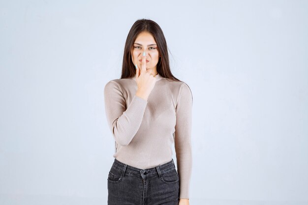 Menina com camisa cinza, apontando para a boca dela.