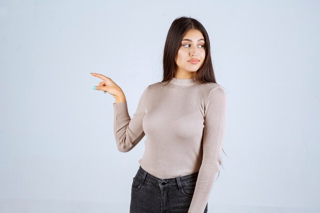 Menina com camisa cinza, apontando para algo à esquerda.