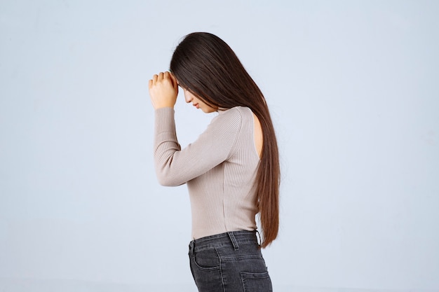 Menina com camisa cinza, unindo as mãos e orando.