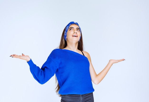 Menina com camisa de festa azul, apontando para algo ao redor.