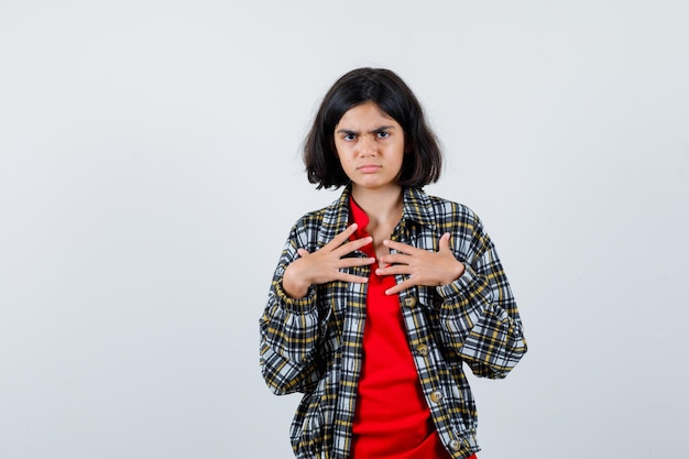 Menina com camisa, jaqueta, apontando para ela mesma e parecendo descontente, vista frontal.