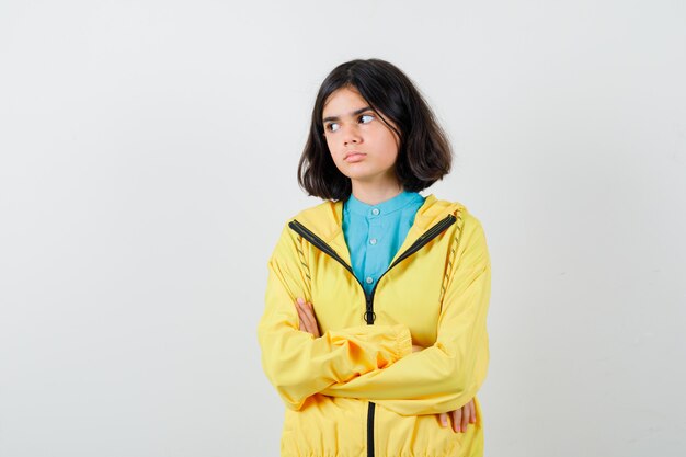 Menina com camisa, jaqueta em pé com os braços cruzados enquanto olha para longe e parece confiante, vista frontal.
