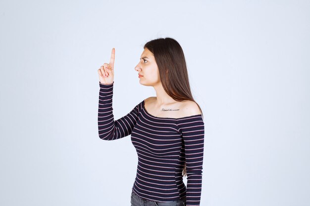 Menina com camisa listrada, apontando para cima e mostrando emoções.