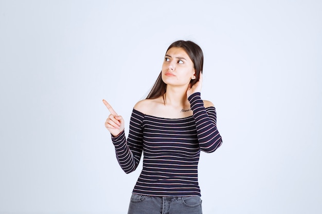 Menina com camisa listrada, apontando para cima e mostrando emoções.