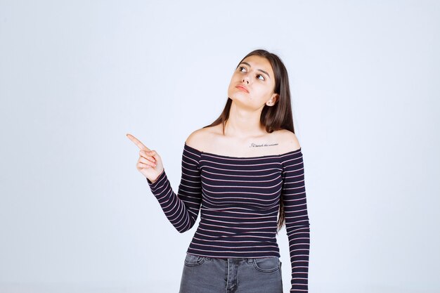 Menina com camisa listrada, apontando para cima e mostrando emoções.