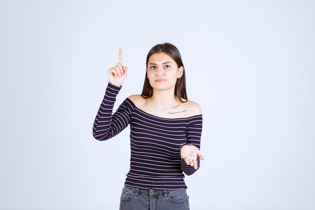 Menina com camisa listrada, apontando para cima e mostrando emoções.