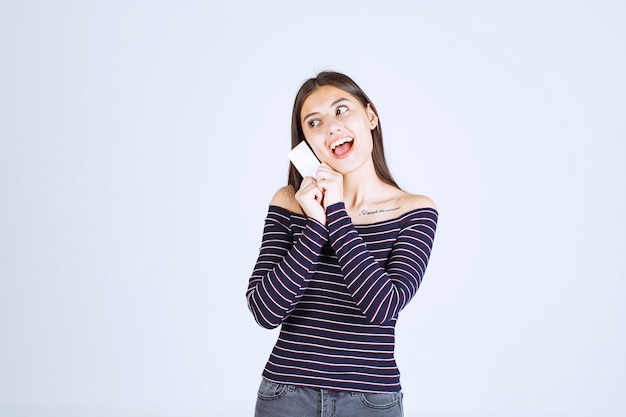 Menina com camisa listrada, apresentando seu cartão de visita com confiança.