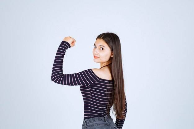 Menina com camisa listrada, demonstrando os músculos do braço.