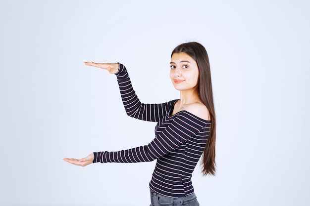 Menina com camisa listrada, mostrando a medida ou quantidade estimada de um produto.