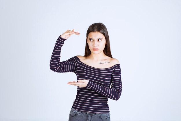 Menina com camisa listrada, mostrando a medida ou quantidade estimada de um produto.