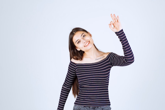 Menina com camisa listrada, mostrando sinal de bom prazer.