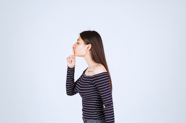 Menina com camisa listrada, pedindo silêncio.