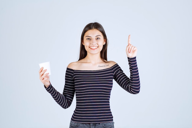 Menina com camisa listrada segurando uma xícara de café de plástico e apresentando-a como um produto.