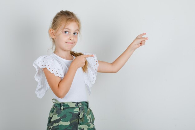 Menina com camiseta branca, saia apontando os dedos e sorrindo