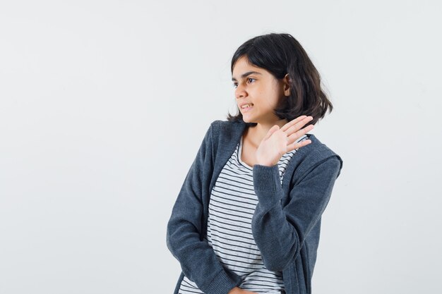 Menina com camiseta e jaqueta acenando com a mão para se despedir e parecendo animada