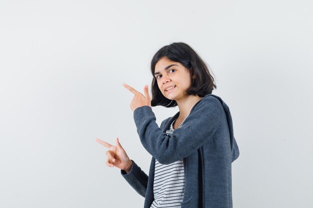 Menina com camiseta, jaqueta apontando para o lado e parecendo curiosa