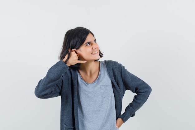 Menina com camiseta, jaqueta mostrando gesto de telefone e parecendo alegre,