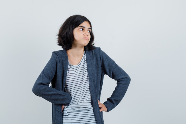 Menina com camiseta, jaqueta olhando para o lado e parecendo hesitante,