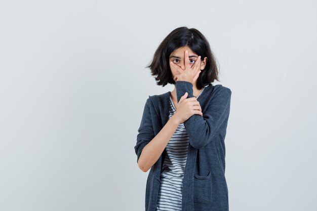 Menina com camiseta, jaqueta olhando por entre os dedos,