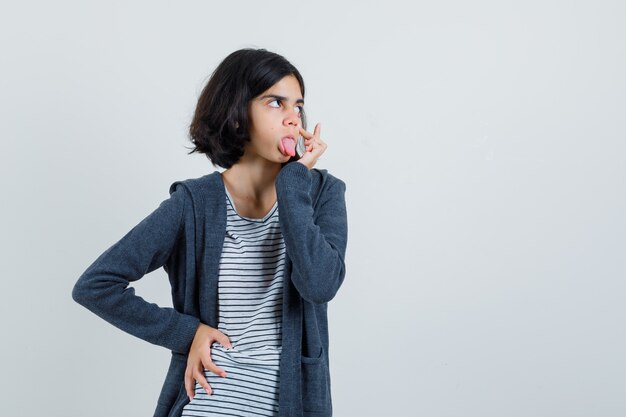 Menina com camiseta, jaqueta puxando a pálpebra, mostrando a língua,