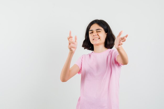 Menina com camiseta rosa apontando para frente, piscando os olhos e parecendo confiante, vista frontal.