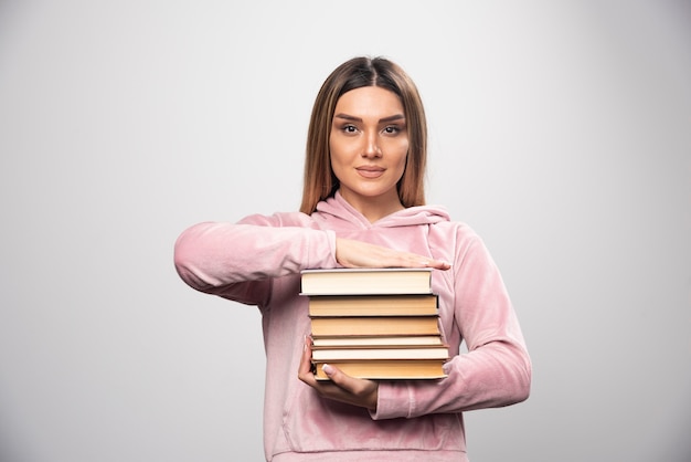 Menina com camiseta rosa segurando e carregando uma pilha pesada de livros