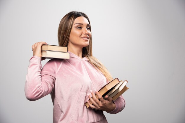 Menina com camiseta rosa segurando os livros por cima do ombro.