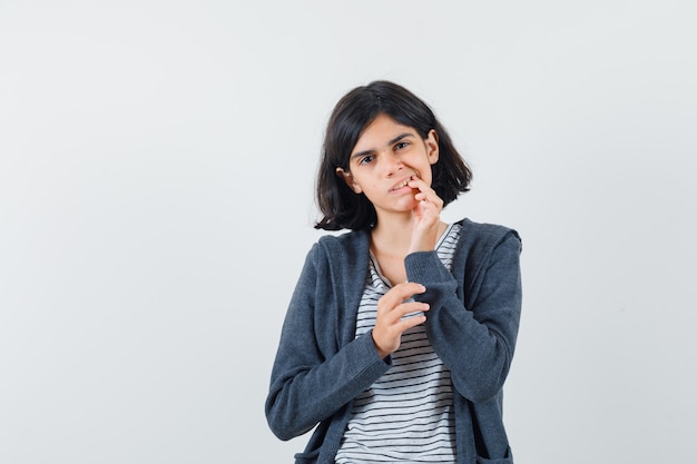 Menina com dor de dente usando camiseta, jaqueta e parecendo desconfortável