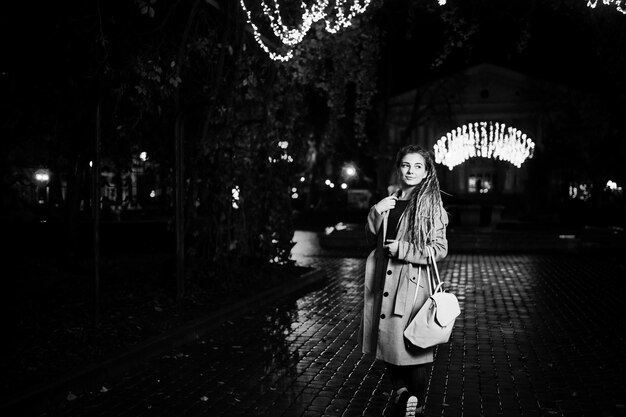 Menina com dreadlocks andando na rua noturna da cidade contra luzes de guirlanda