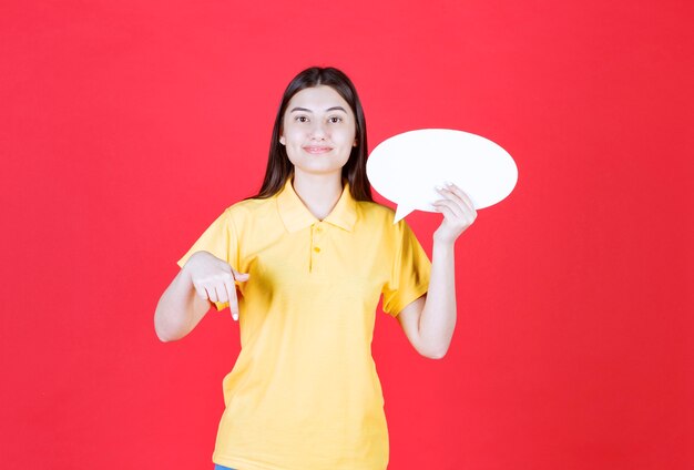 Menina com dresscode amarelo segurando um quadro oval de informações e ligando para alguém ao lado dela