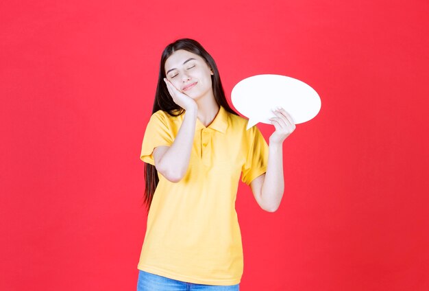 Menina com dresscode amarelo segurando um quadro oval de informações e parece sonolenta e cansada