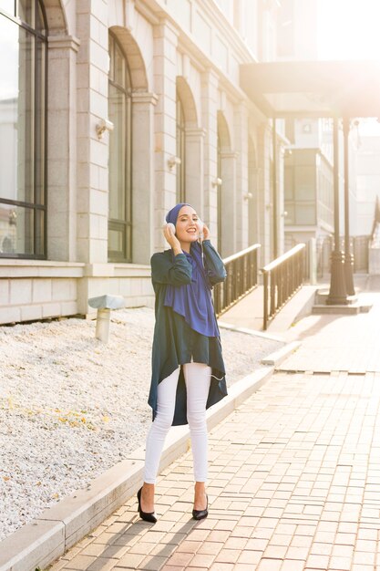 Menina com hijab ouvindo música com fones de ouvido do lado de fora