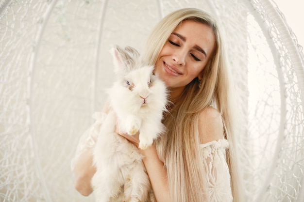 Menina com longos cabelos loiros com um coelho branco nos braços.