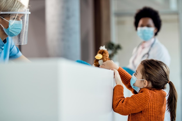 Foto grátis menina com máscara facial protetora falando com uma enfermeira na recepção do hospital