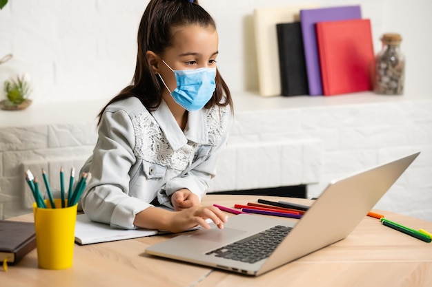 Menina com máscara médica estudando em casa. epidemia, pandemia.