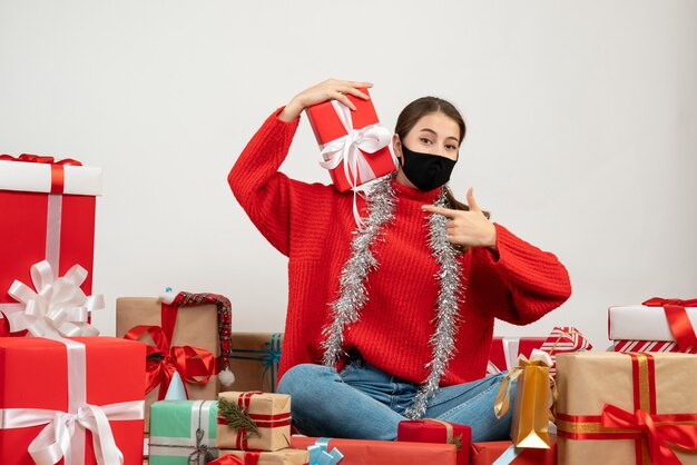 menina com máscara preta apontando para o momento sentada em volta de presentes