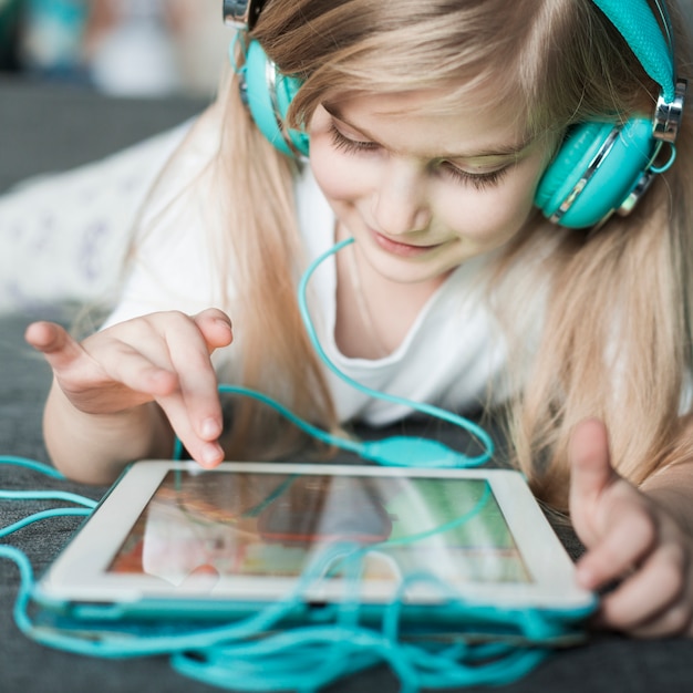 Menina com o tablet tocando nos fones de ouvido