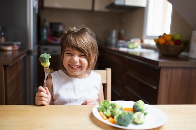 Menina com os olhos fechados comendo legumes