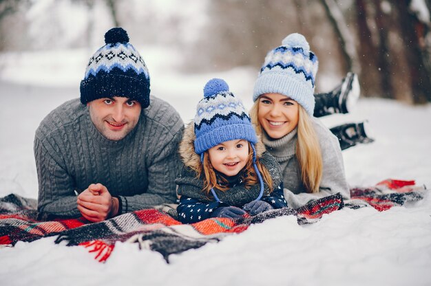 Menina com os pais sentados em um cobertor em um parque de inverno