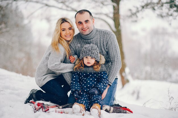 Menina com os pais sentados em um cobertor em um parque de inverno