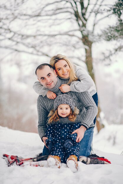 Menina com os pais sentados em um cobertor em um parque de inverno