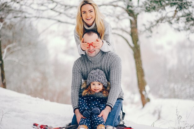 Menina com os pais sentados em um cobertor em um parque de inverno