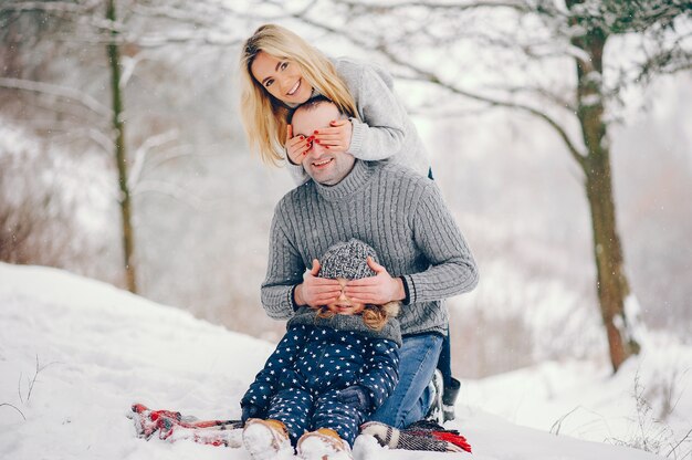 Menina com os pais sentados em um cobertor em um parque de inverno