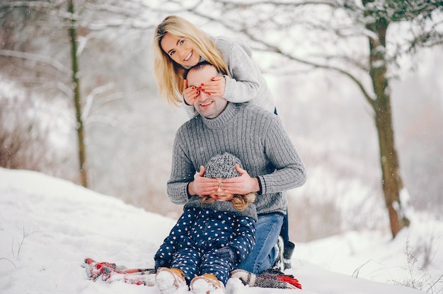 Menina com os pais sentados em um cobertor em um parque de inverno