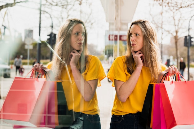 Menina com sacolas de compras, olhando para o seu reflexo