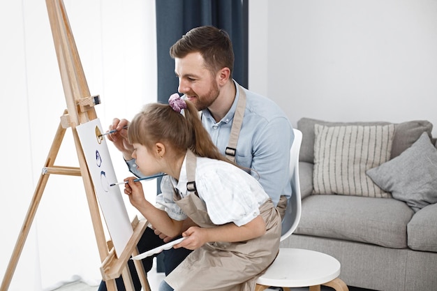 Menina com síndrome de Down e seu pai pintando em um cavalete com pincéis