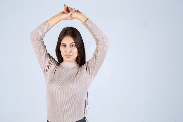 Menina com suéter cinza dando poses desagradáveis e sedutoras.