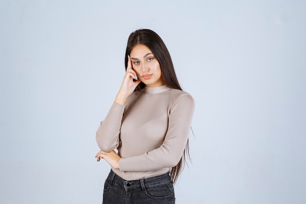 Menina com suéter cinza dando poses desagradáveis e sedutoras.