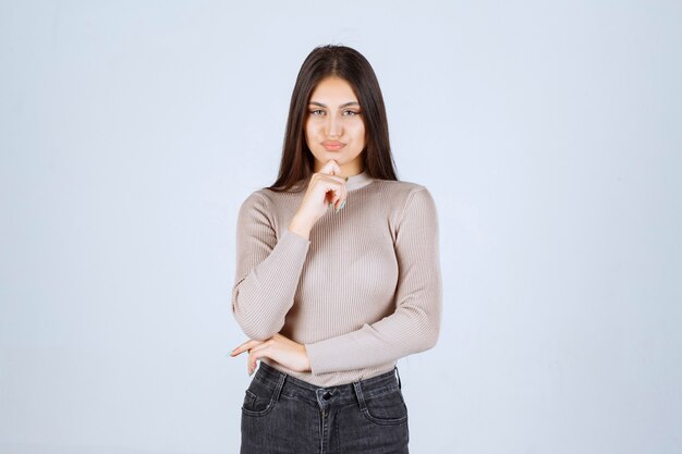 Menina com suéter cinza dando poses desagradáveis e sedutoras.